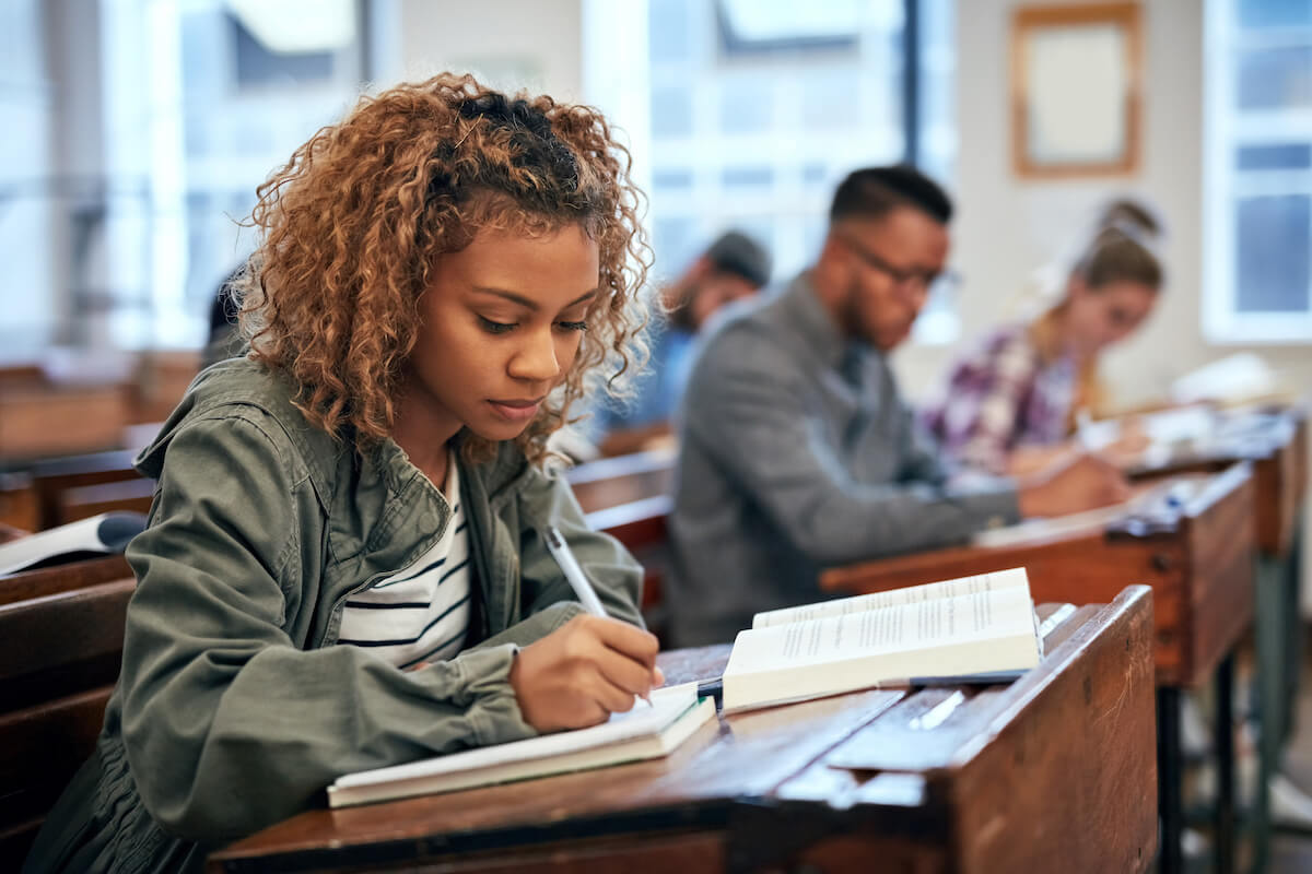 women sitting at old desk copying notes from textbook