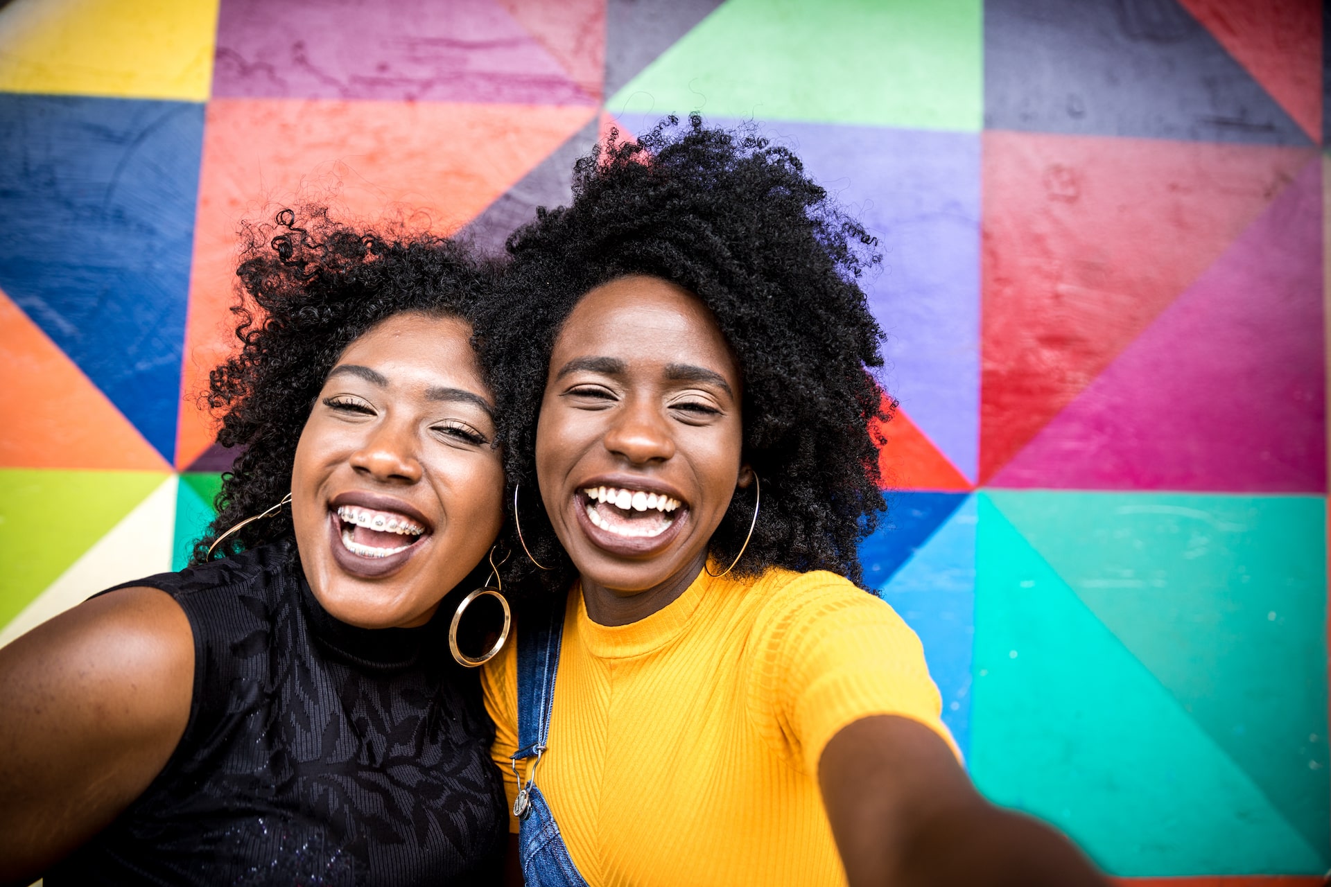 two women smiling and laughing in front of colorful wall