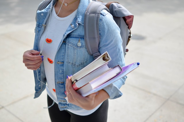 young woman wearing a blue denim jacket while holding books